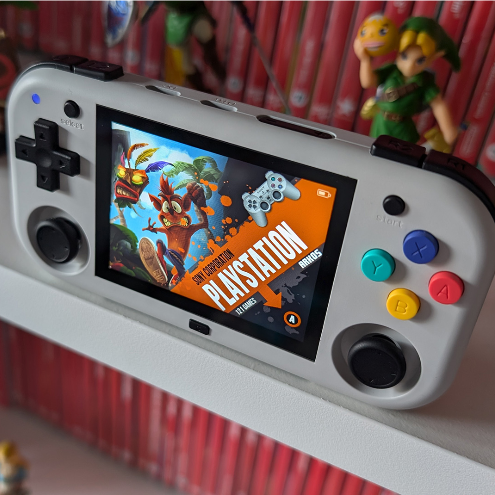 Handheld gaming console with colorful buttons and a PlayStation game on screen, with toys in the background.